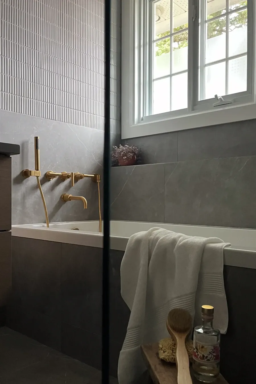 Brass sconce detail on fluted porcelain tile — walnut drawer fronts below, Boucherville bathroom.