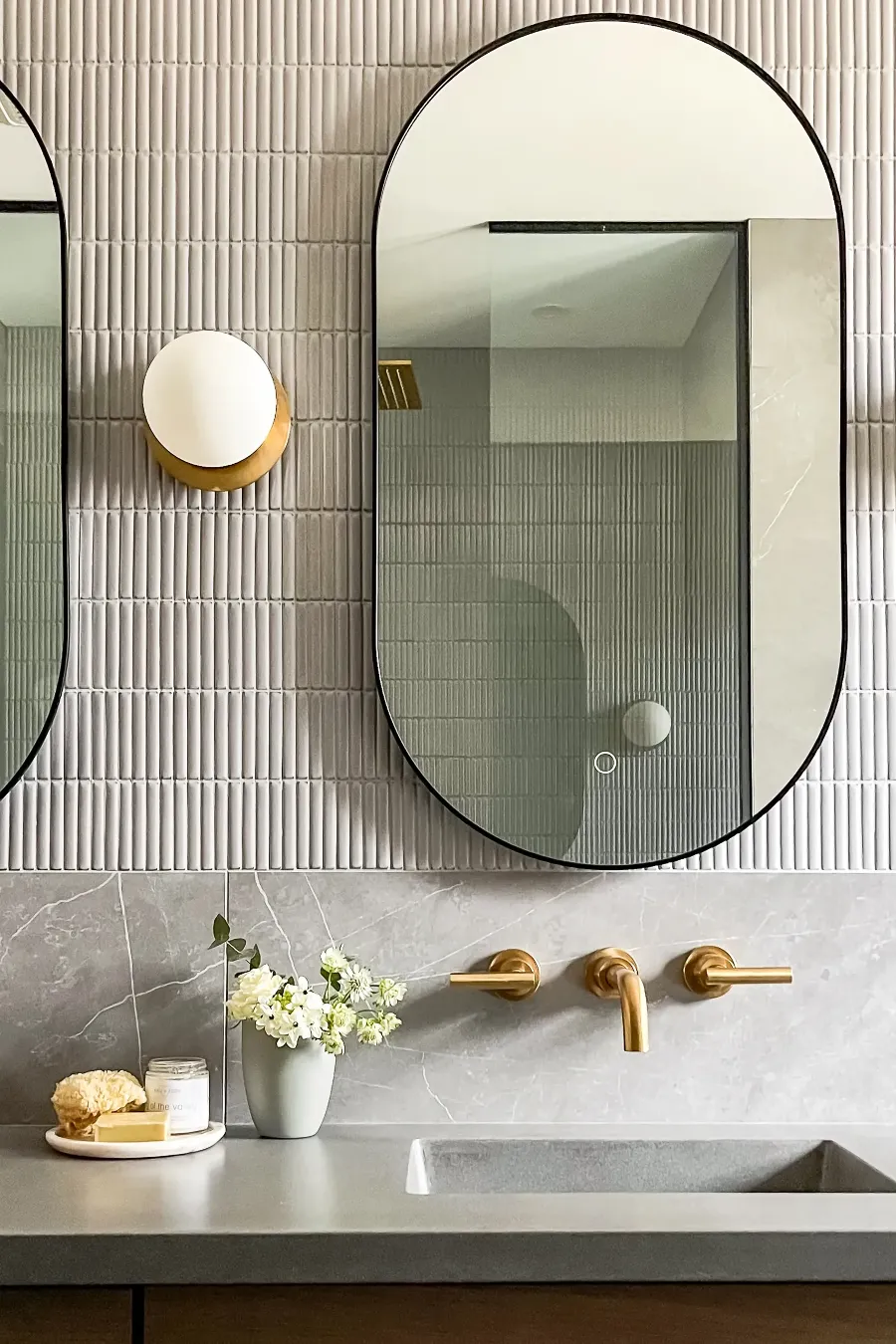 Glass shower and wood bench in the Boucherville primary bathroom — continuous grey stone flooring.