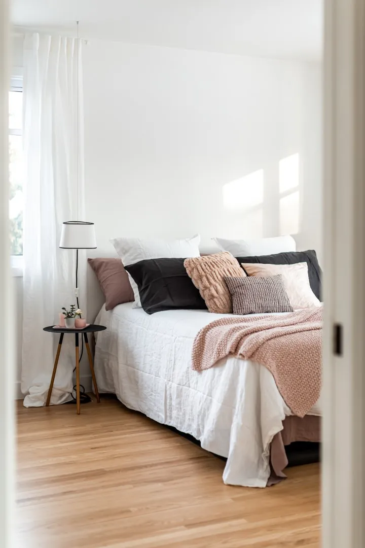 Primary bedroom in the Montreal bungalow — low-profile bed, warm linens, soft pendant at the window.
