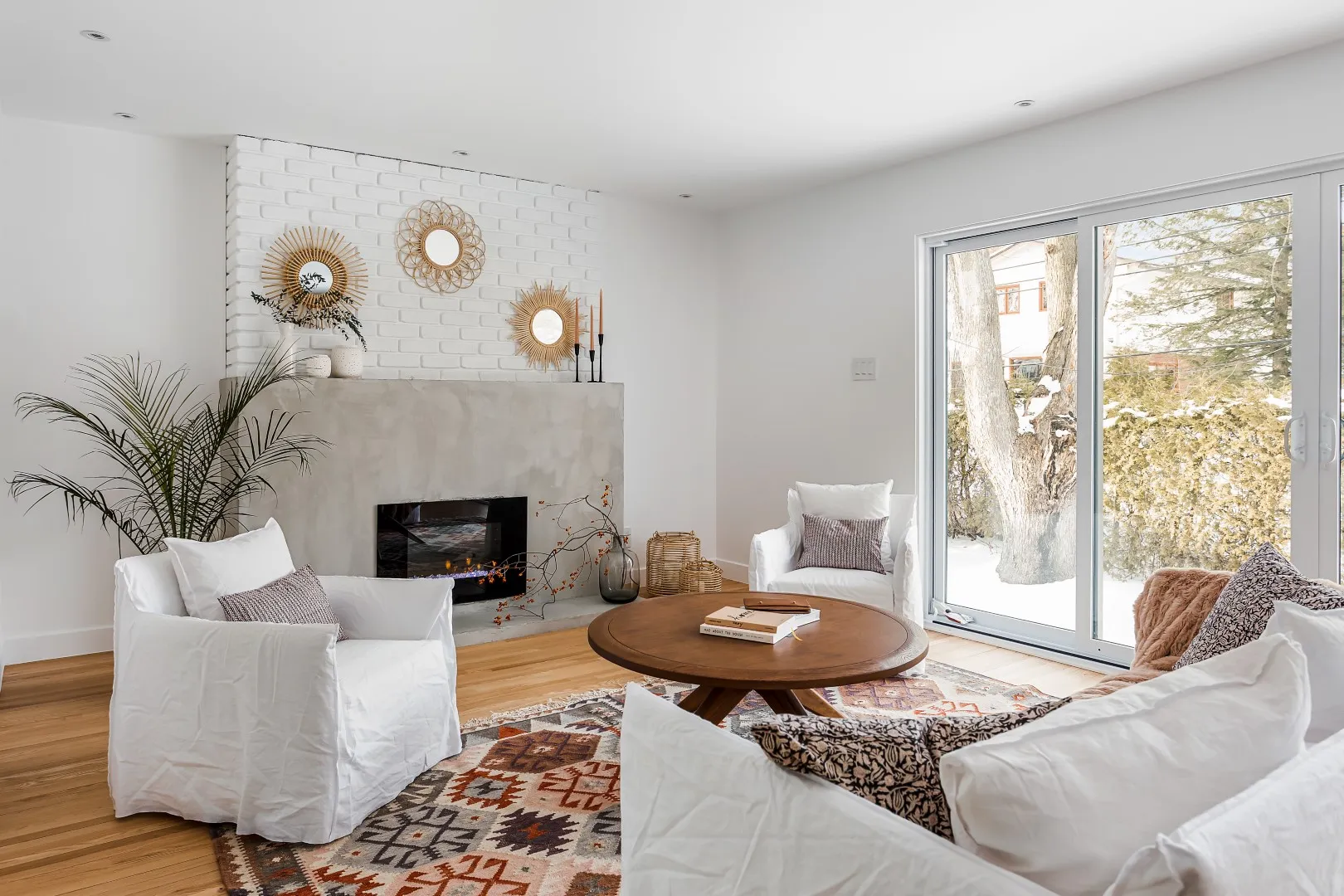 Open living room in the Montreal bungalow — slipcovered sofas, round wood coffee table, glass-panel stair.