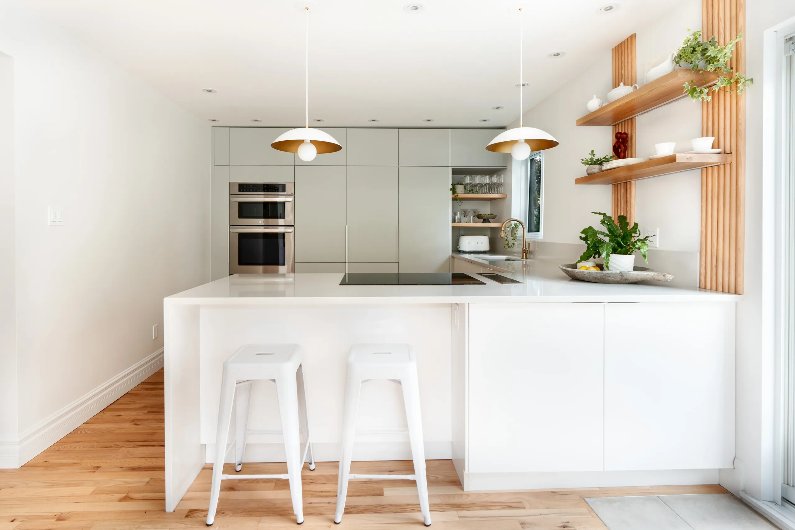 White lacquered U-shape kitchen with oak slatted shelving and low brass pendants — Longueuil remodel.