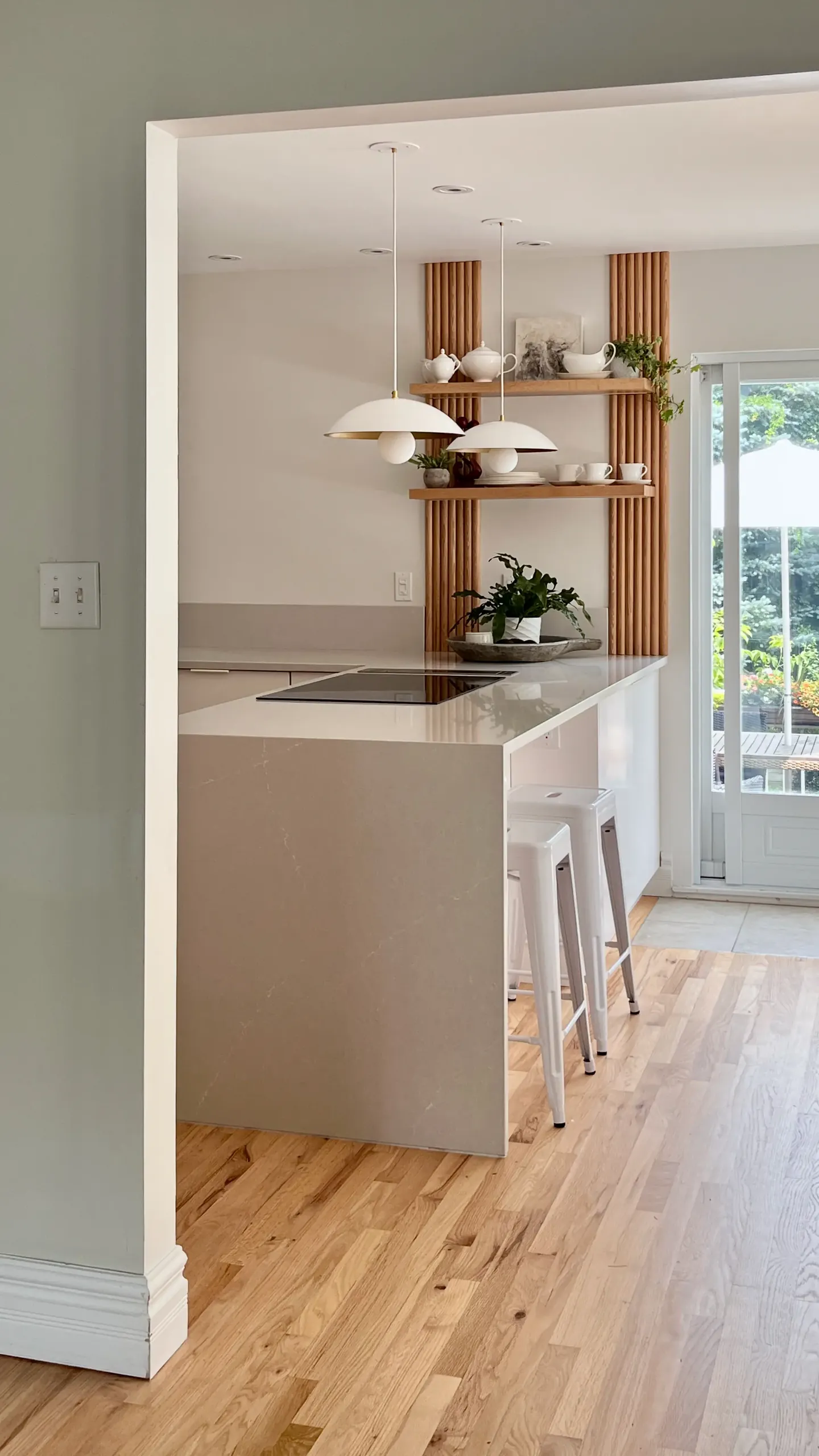 View into the remodeled Longueuil kitchen — oak-slat feature wall, dome pendants, and a soft stone peninsula.
