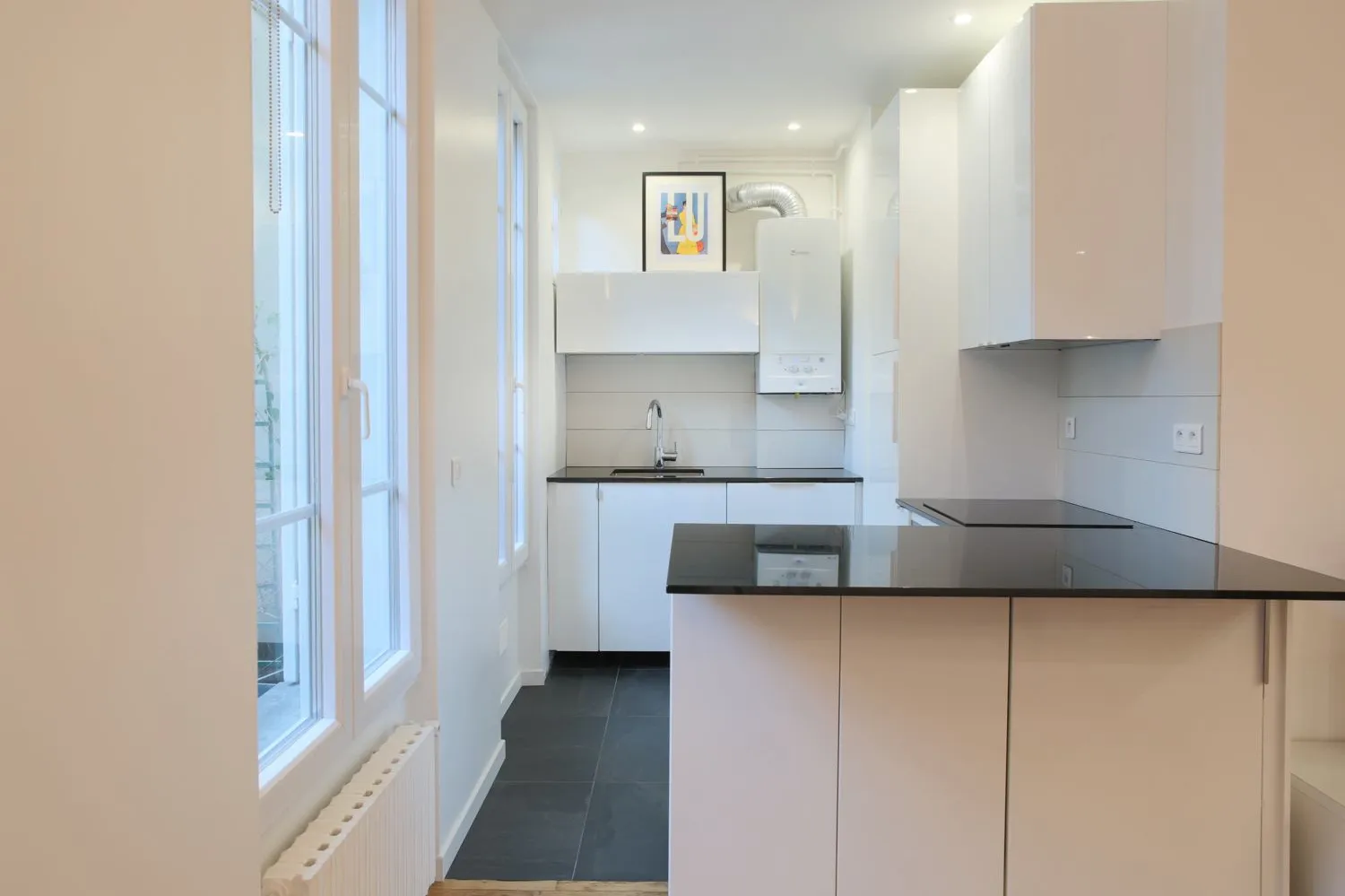 Cuisine compacte dans la location du Paris 16e — ébénisterie blanche et plancher de chêne rafraîchi.