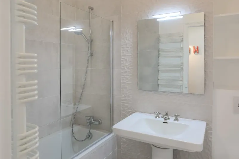 Salle de bain réaménagée dans la location du Paris 16e — accessoires épurés, céramique neutre.